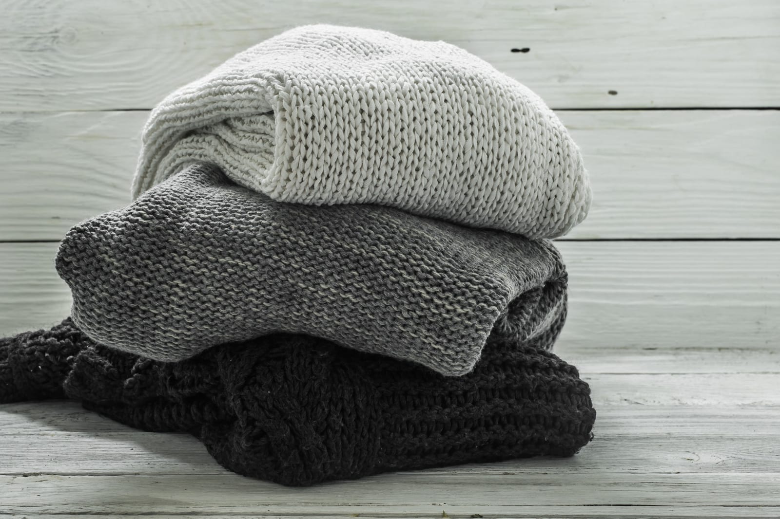 Drei gestrickte Pullover in Schwarz, Grau und Weiss